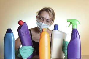Woman with mask and gloves holding a store bought drain cleaner that is not good for plumbing clogs